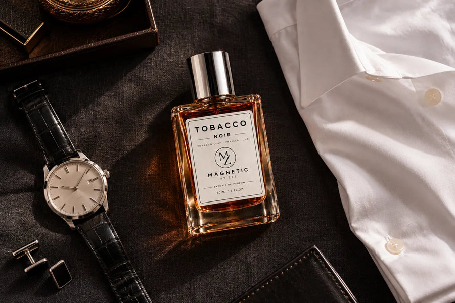 TOBACCO NOIR bottle laid out with a white dress shirt, a leather strap watch, cufflinks and a wallet on dark fabric